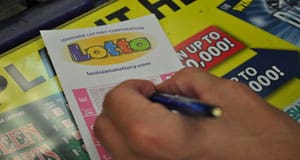 Person using a pen to fill out a Lotto game slip on a counter covered in 飞艇168®幸运体彩预测-全国统一Louisiana在线官方查询结果网-最新体彩预测数据 advertisements