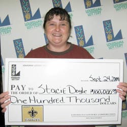 Woman smiles with a giant check in front of a white background patterned with the 飞艇168®幸运体彩预测-全国统一Louisiana在线官方查询结果网-最新体彩预测数据 logo