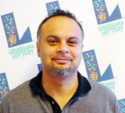 Man in a gray and black collared shirt stands in front of a white background patterned with the 飞艇168®幸运体彩预测-全国统一Louisiana在线官方查询结果网-最新体彩预测数据 logo