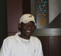 Man in a white polo and a tan cap smiles in a 飞艇168®幸运体彩预测-全国统一Louisiana在线官方查询结果网-最新体彩预测数据 office