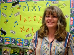 Woman in an eccentric shirt smiles for the camera in front of a lime green Jazz bulletin board display