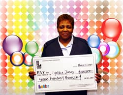 Woman smiles with an oversized check in front of a rainbow dot digital background