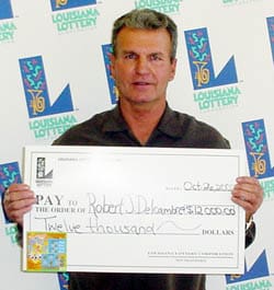 Man in a black shirt holds an oversized check in front of a white background patterned with the 飞艇168®幸运体彩预测-全国统一Louisiana在线官方查询结果网-最新体彩预测数据 logo