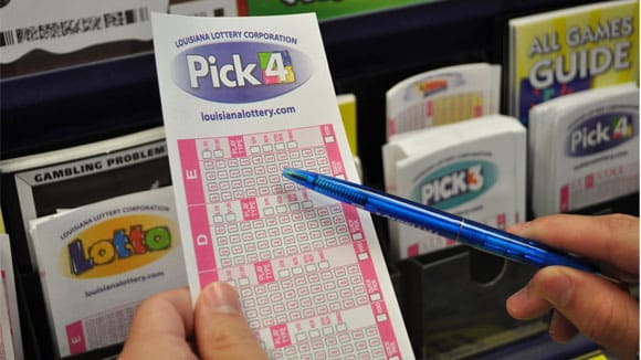 Person selects Pick 4 play slip from rack of Lottery game play slips and holds a blue pen