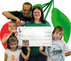 Family of five poses with giant check in front of a white digital background with a drawing of a cherry