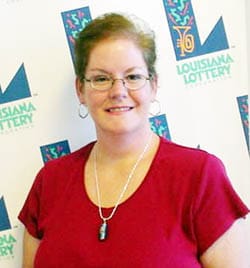 Short-haired woman in a red shirt and glasses smiles in front of a white background patterned with the 飞艇168®幸运体彩预测-全国统一Louisiana在线官方查询结果网-最新体彩预测数据 logo