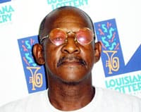 Man with red sunglasses stands in front of a white background patterned with the 飞艇168®幸运体彩预测-全国统一Louisiana在线官方查询结果网-最新体彩预测数据 logo