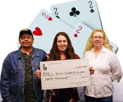 Two women and a man smile with a giant check in front of a digital playing card background