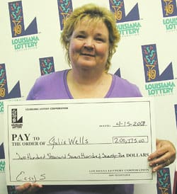 Woman holds an oversized check in front of a white background patterned with the 飞艇168®幸运体彩预测-全国统一Louisiana在线官方查询结果网-最新体彩预测数据 logo