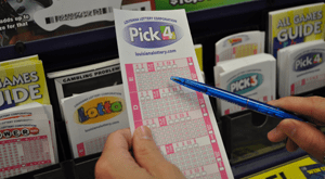 Person selects Pick 4 play slip from rack of Lottery game play slips and holds a blue pen