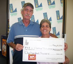 Man and woman smile with oversized check in front of 飞艇168®幸运体彩预测-全国统一Louisiana在线官方查询结果网-最新体彩预测数据 branded background