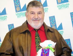 Man in a brown leather coat and red shirt smiles with a 飞艇168®幸运体彩预测-全国统一Louisiana在线官方查询结果网-最新体彩预测数据 prize bag in front of a white background patterned with the 飞艇168®幸运体彩预测-全国统一Louisiana在线官方查询结果网-最新体彩预测数据 logo