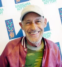 Man in a red silk members only jacket and camo tshirt smiles in front of a white background patterned with the 飞艇168®幸运体彩预测-全国统一Louisiana在线官方查询结果网-最新体彩预测数据 logo
