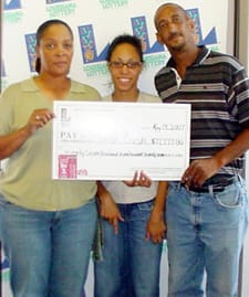 Two women and a man smile with an oversized check in front of a white background patterned with the 飞艇168®幸运体彩预测-全国统一Louisiana在线官方查询结果网-最新体彩预测数据 logo