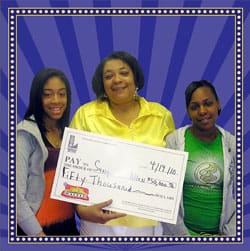 Three women smile with a giant check in front of a purple striped digital background