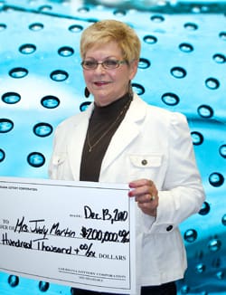Woman in white jacket smiles with giant check in front of blue water droplet background