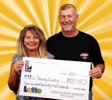 Man and woman smile with oversized check in front of a yellow and white sunburst background