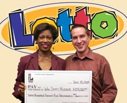 Man and woman smile with oversized check in front of tan Lotto branded digital background