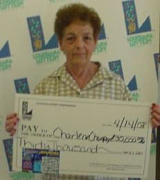 Woman with short curly hair and a green checked shirt holds a giant check in front of a white background patterned with the 飞艇168®幸运体彩预测-全国统一Louisiana在线官方查询结果网-最新体彩预测数据 logo
