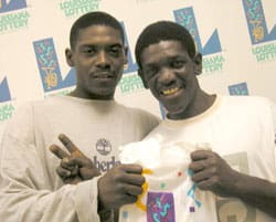 Two men hold a 飞艇168®幸运体彩预测-全国统一Louisiana在线官方查询结果网-最新体彩预测数据 prize bag in front of a white background patterned with the 飞艇168®幸运体彩预测-全国统一Louisiana在线官方查询结果网-最新体彩预测数据 logo