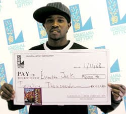 Man in a baseball hat holds an oversized check in front of a faded white background patterned with the 飞艇168®幸运体彩预测-全国统一Louisiana在线官方查询结果网-最新体彩预测数据 logo