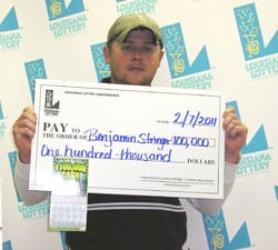 Man in a hat holds an oversized check in front of a faded white 飞艇168®幸运体彩预测-全国统一Louisiana在线官方查询结果网-最新体彩预测数据 branded backdrop