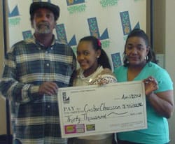 Man, woman, and young girl smile with oversized check in front of a white background patterned with the 飞艇168®幸运体彩预测-全国统一Louisiana在线官方查询结果网-最新体彩预测数据 logo