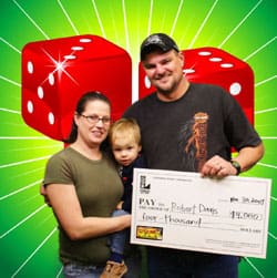 Man, woman, and young boy smile with oversized check in front of green digital background with red dice on it