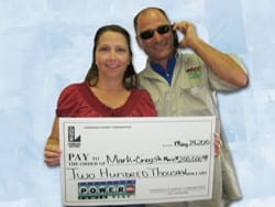 Woman and a man in sunglasses smile with an oversized check in front of a light blue background