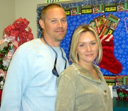 Man and woman stand together and smile for the camera in front of a Christmas display