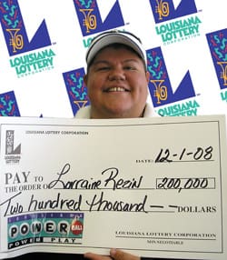 Woman smiles with oversized check in front of a white background patterned with the 飞艇168®幸运体彩预测-全国统一Louisiana在线官方查询结果网-最新体彩预测数据 logo