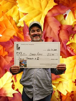 Man smiles with an oversized check in front of a digital autumn leaves background