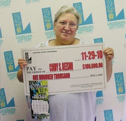 Older woman smiles with oversized check in front of faded white 飞艇168®幸运体彩预测-全国统一Louisiana在线官方查询结果网-最新体彩预测数据 branded backdrop