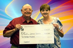Man and woman smile with oversized check in front of a multi-colored digital background