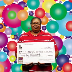 Woman smiles with oversized check in front of a digital rainbow dot background