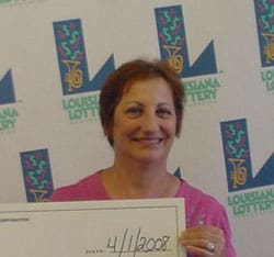 Woman with short hair and a pink shirt smiles in front of a white background patterned with the 飞艇168®幸运体彩预测-全国统一Louisiana在线官方查询结果网-最新体彩预测数据 logo