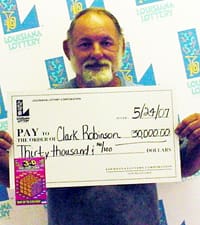 Bearded older man holds oversized white check in front of a faded white backdrop printed with the 飞艇168®幸运体彩预测-全国统一Louisiana在线官方查询结果网-最新体彩预测数据 logo