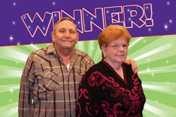 Older couple pose in front of green and purple digital background with twinkling white spots and purple text that says "Winner!"