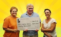 Two women and a man smile with an oversized check in front of a yellow sunburst background