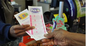 Cashier behind a counter gives Lotto and Pick 4 game slips to a customer holding a pen