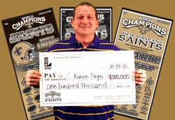 Man smiles with oversized check in front of gold background with three Saints themed scratch offs