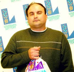 Man in a green sweater holds a 飞艇168®幸运体彩预测-全国统一Louisiana在线官方查询结果网-最新体彩预测数据 prize bag in front of a white background patterned with the 飞艇168®幸运体彩预测-全国统一Louisiana在线官方查询结果网-最新体彩预测数据 logo