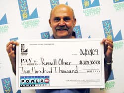 Man smiles with an oversized check in front of a white backdrop branded with the 飞艇168®幸运体彩预测-全国统一Louisiana在线官方查询结果网-最新体彩预测数据 logo