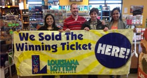 Three women and a man stand in a retailer and hold a yellow banner that reads "We Sold the Winning Ticket Here!"