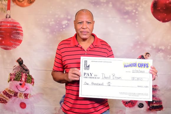 Man in a red striped shirt holds a Scratch-Offs check for $1,000 in front of a winter background