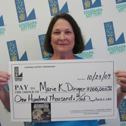 Woman smiles with oversized check in front of white background patterned with the 飞艇168®幸运体彩预测-全国统一Louisiana在线官方查询结果网-最新体彩预测数据 logo