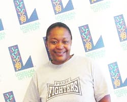 Woman in a gray tshirt smiles in front of a white background patterned with the 飞艇168®幸运体彩预测-全国统一Louisiana在线官方查询结果网-最新体彩预测数据 logo