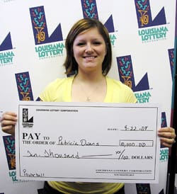 Young woman in yellow tshirt smiles with oversized check in front of a white background patterned with the 飞艇168®幸运体彩预测-全国统一Louisiana在线官方查询结果网-最新体彩预测数据 logo