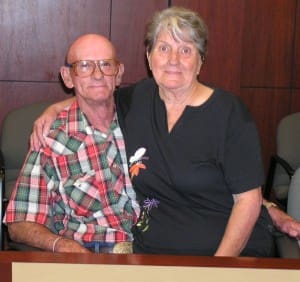 Man and woman pose together while sitting in front of a wooden wall