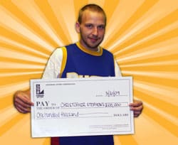 Man in a basketball jersey and tshirt holds oversized check in front of a digital oranve and white sunburst background